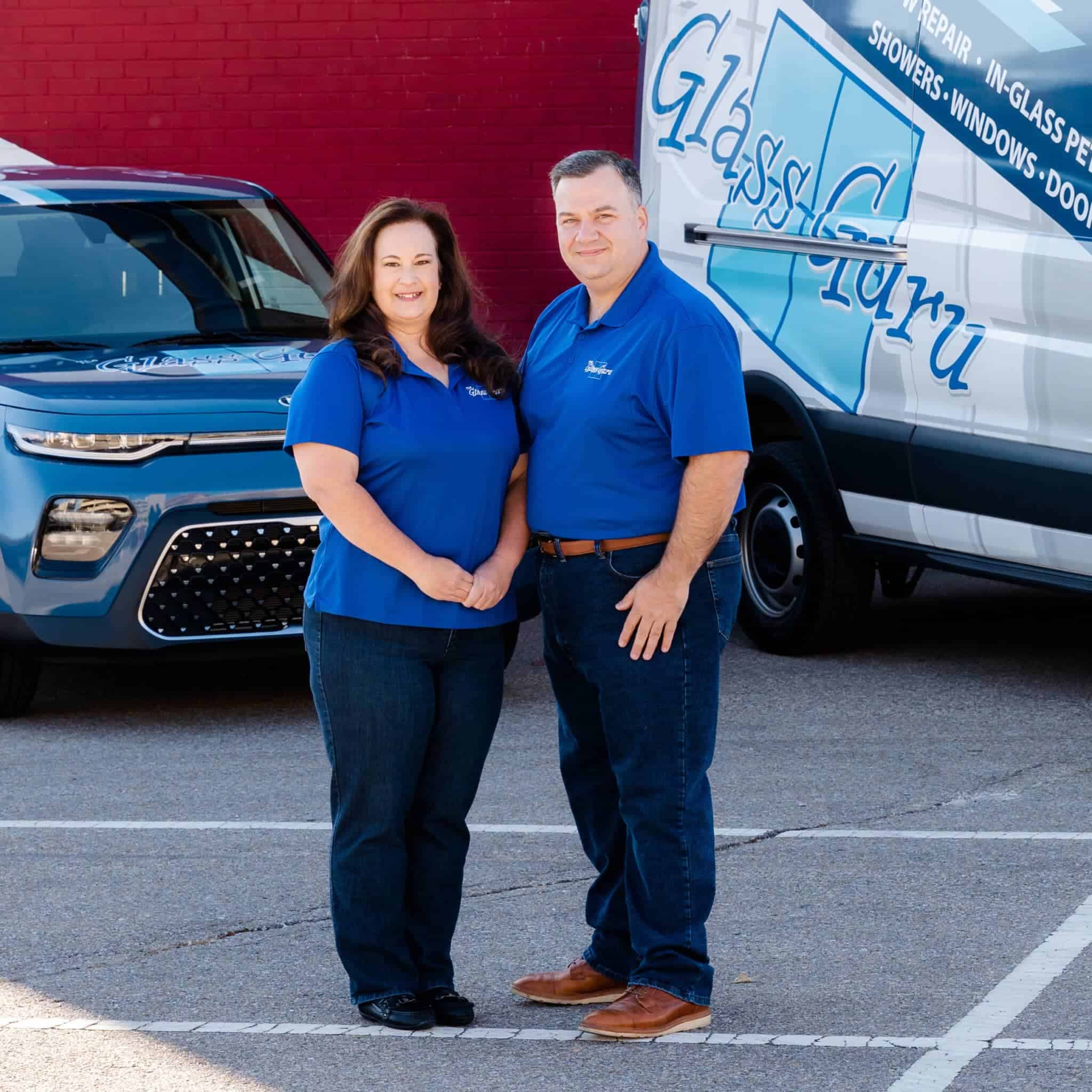 Two people in blue shirts standing in front of a van.