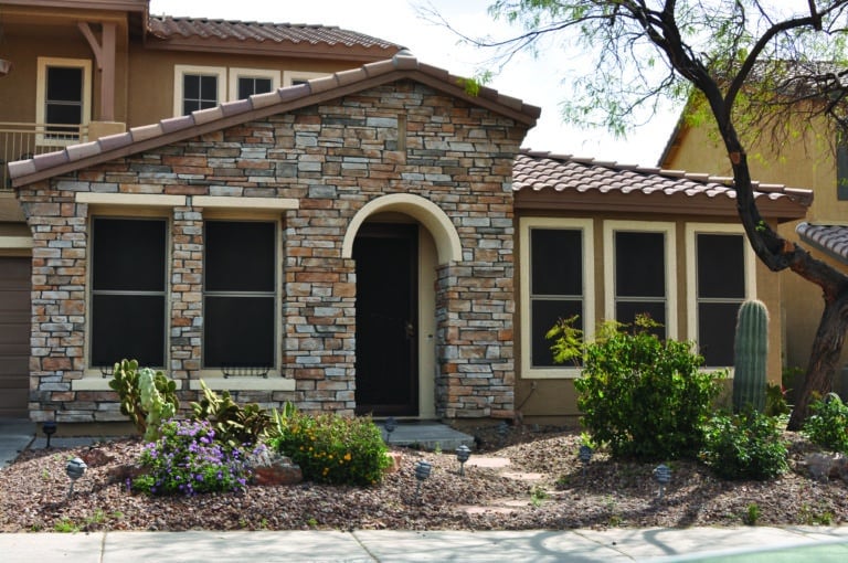 A solar screens-covered house with a cactus in front of it.