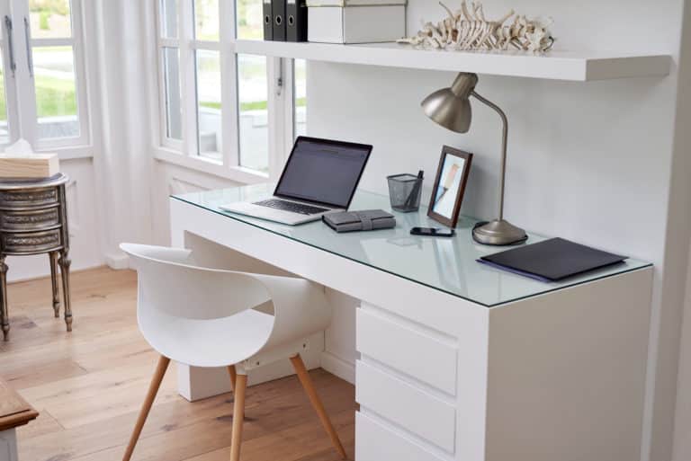 A white desk with a glass desktop, a laptop, and a chair.