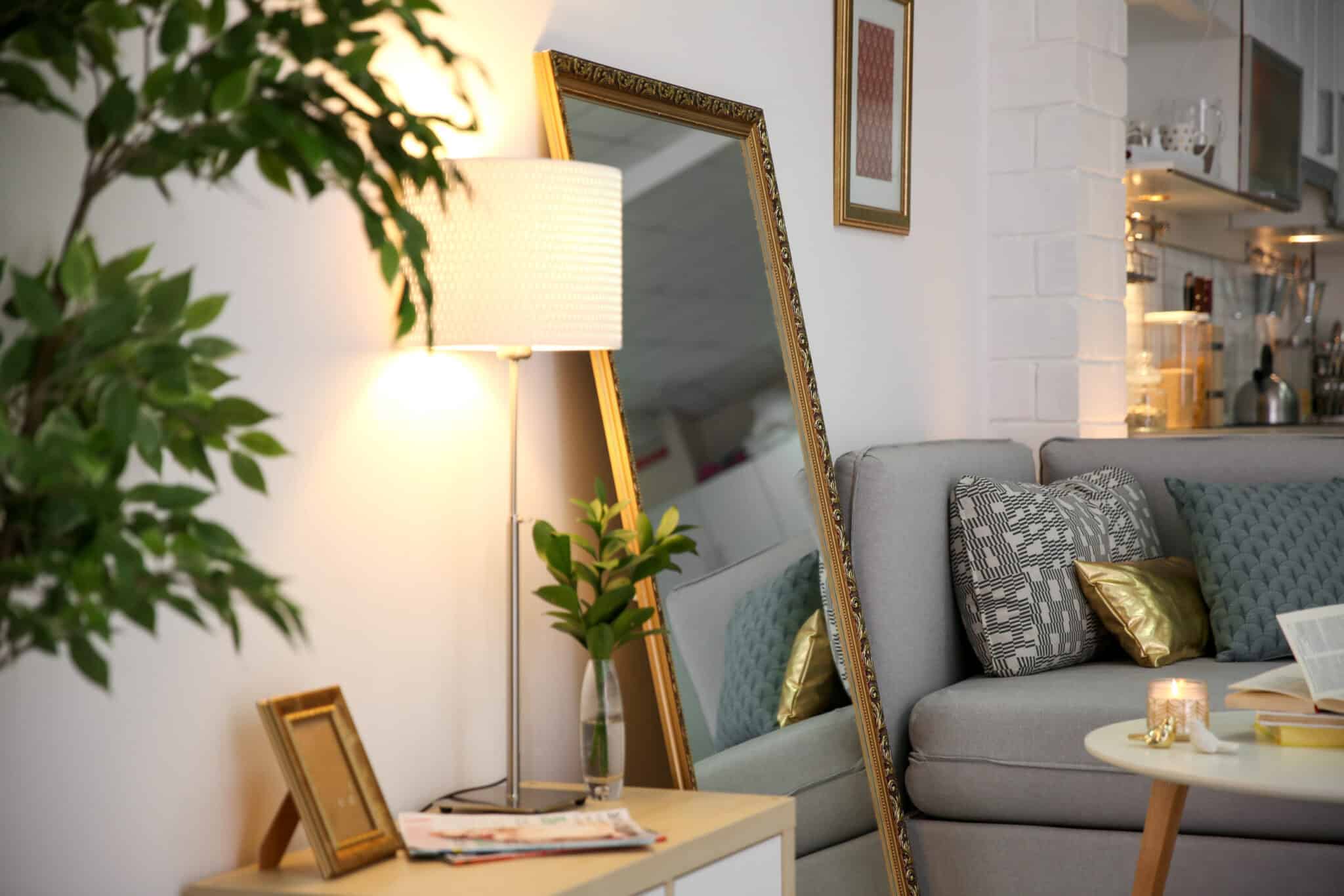 A living room with a couch adorned with decorative pillows and a stylish mirror hung on the wall.