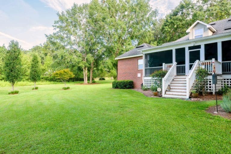 A home with a brick front porch and grassy yard featuring screens for added comfort.