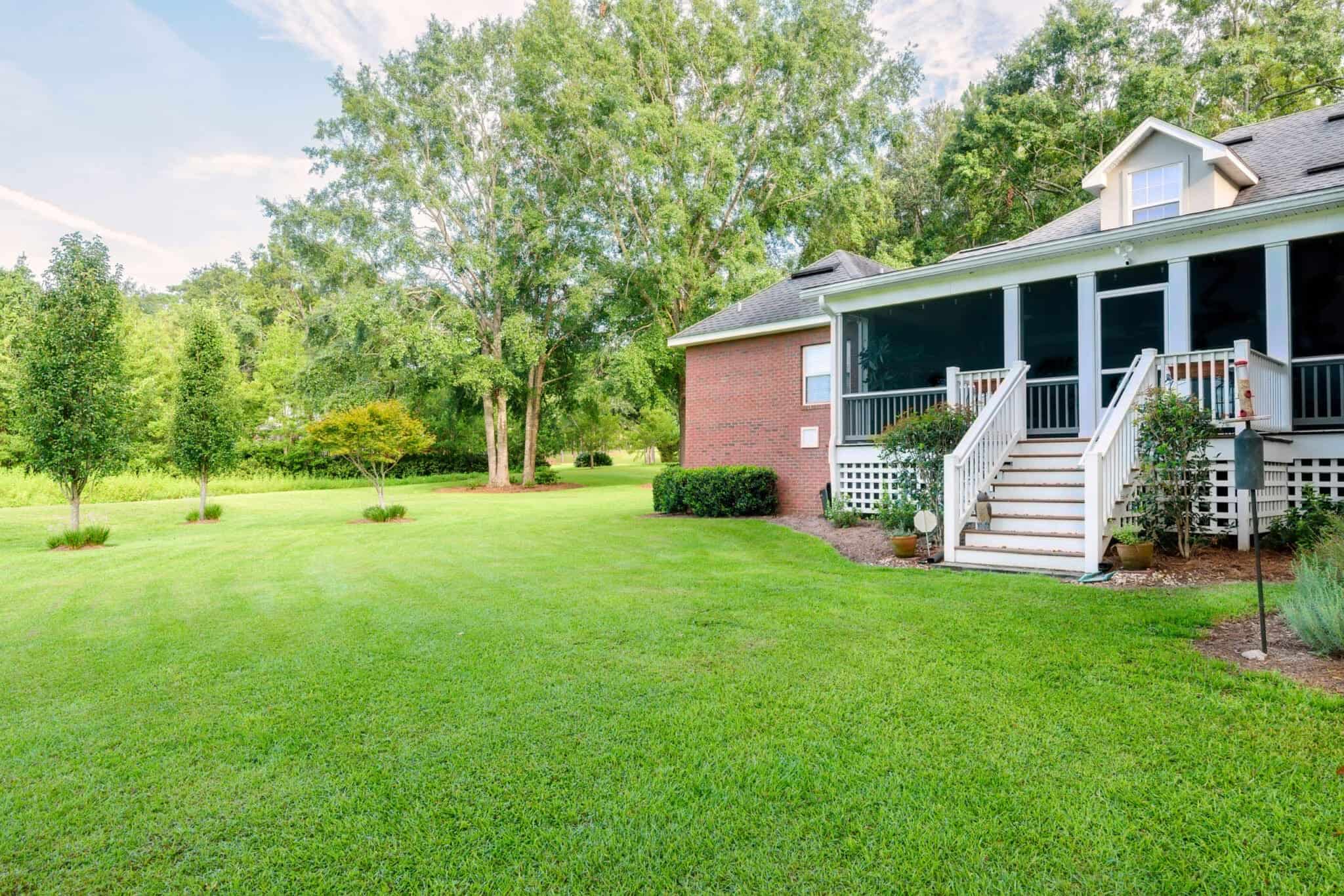 A home with a brick front porch and grassy yard featuring screens for added comfort.