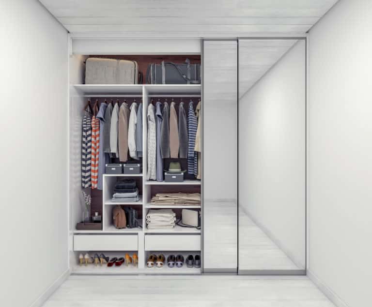 A white closet with mirrored doors and clothes.