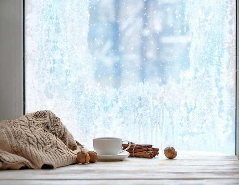 A cup of coffee on a wooden table next to a window, providing a cozy ambiance and a view outside.