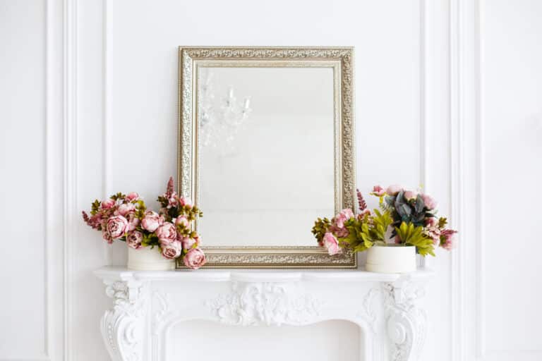 A white fireplace adorned with elegant flowers and a sleek mirror, reflecting the latest in mirror trends.