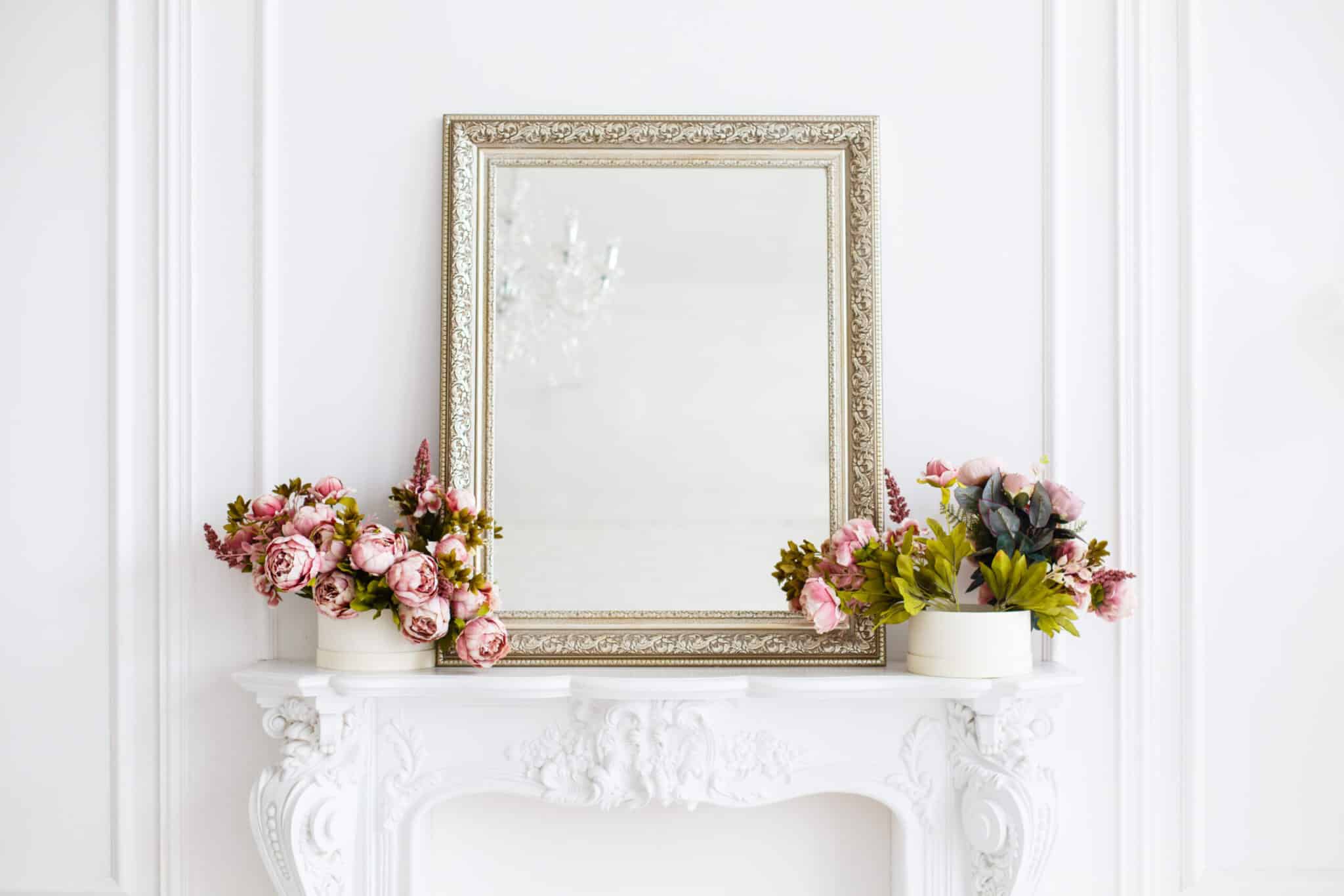 A white fireplace adorned with elegant flowers and a sleek mirror, reflecting the latest in mirror trends.